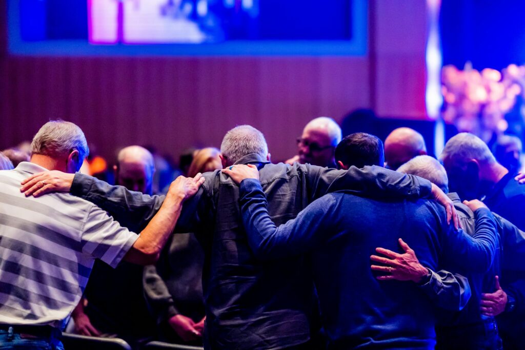 A congregation of men embracing and praying together in a church setting.
