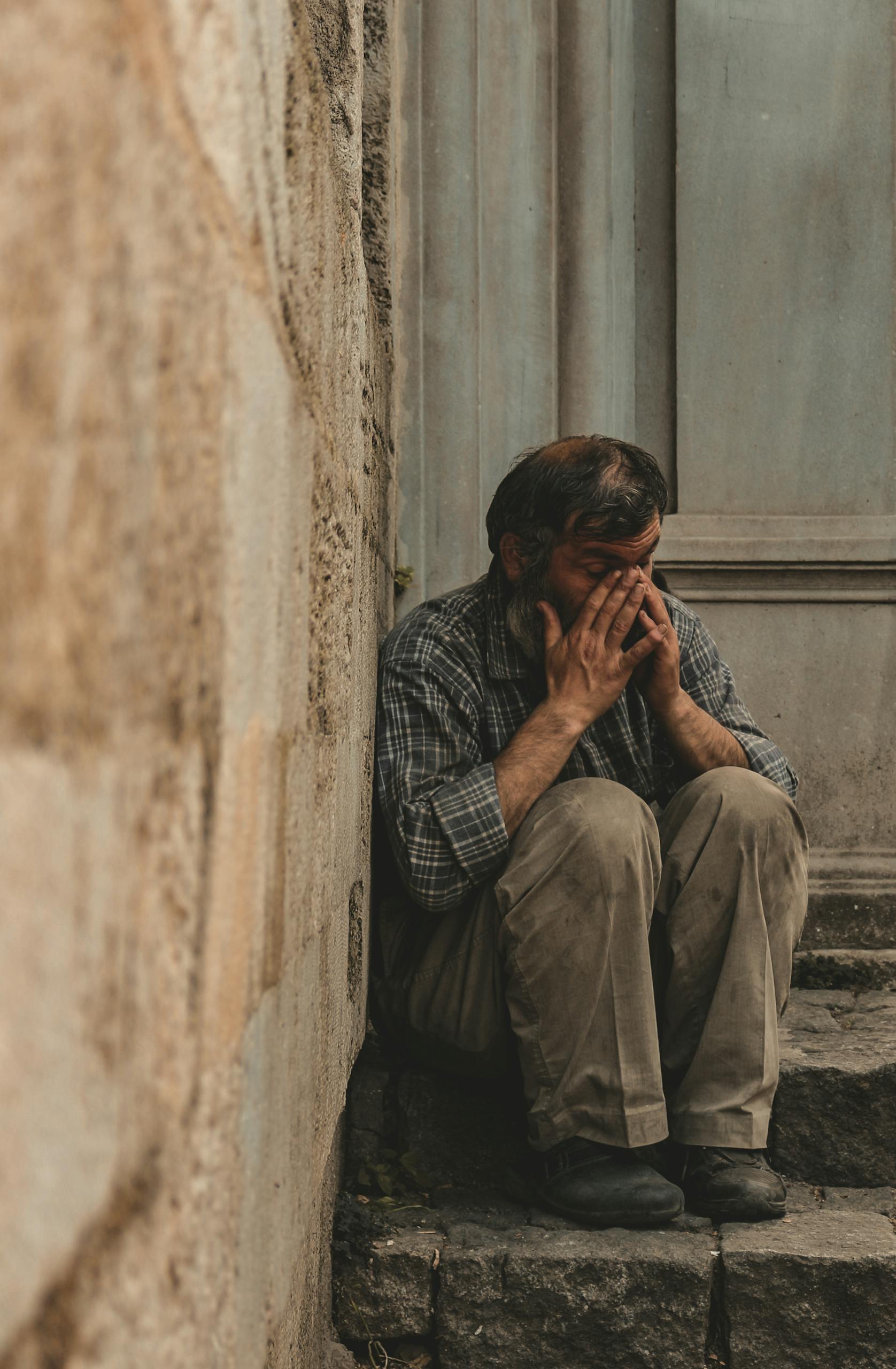 A contemplative man sits on stone stairs in an urban setting, appearing thoughtful and reflective.